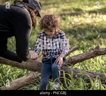 Madre aiuta a little boy dopo che egli ha fatto male la sua mano, donna frequentando il ragazzino di raschiare Foto Stock