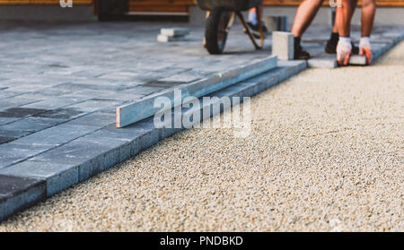 La posa di cemento grigio Pavimentazioni in casa cortile carraio patio. I lavoratori professionali di muratori sta installando nuove piastrelle o lastre per passo carraio, Foto Stock