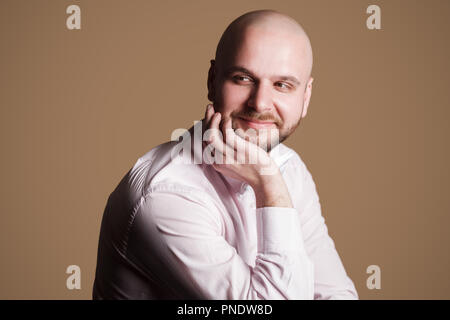 Ritratto di successo bello barbuto uomo calvo in luce maglia rosa e bianco bow, seduti su una sedia e guardando lontano con faccina sorridente e meditare. Foto Stock