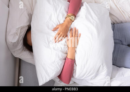 Elevato angolo di visione della donna azienda cuscino bianco oltre il suo volto Foto Stock