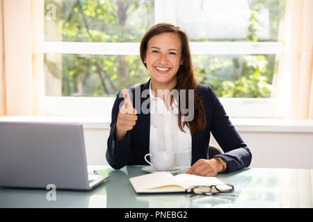 Ritratto di un felice giovane imprenditrice gesticolando Thumbs up in Office Foto Stock