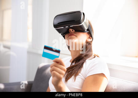 Giovane donna con carta di credito indossando occhiali per realtà virtuale Foto Stock