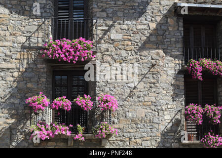 Una vista frontale di una facciata in pietra con quattro black ringhiera in ferro balconi con violetta floreali pendenti su di essi in Ainsa , un piccolo villaggio rurale in Spagna Foto Stock