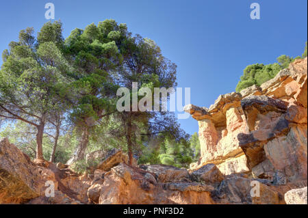 Un rosso sporgente roccia con alberi e un profondo cielo blu in stile canyon colline di Anento, una piccola cittadina in Aragona, Spagna Foto Stock