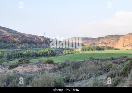 Un paesaggio rurale con coltivate e i campi di erba accanto al fiume Aguavivas, al tramonto, con alcune colline sullo sfondo, in Aragona, Spagna Foto Stock