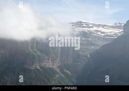 Un paesaggio di alta montagna e massicci, pini e abeti di foresta e un profondo cielo blu con alcune nuvole in Ordesa Valley (Valle de Ordesa), Spagna Foto Stock