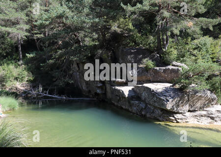 Un piccolo stagno circondato da abeti e pini su grossi massi di roccia sul fiume Arba, accanto a Luesia, un piccolo e tipico paese situato in Aragona, Spagna Foto Stock