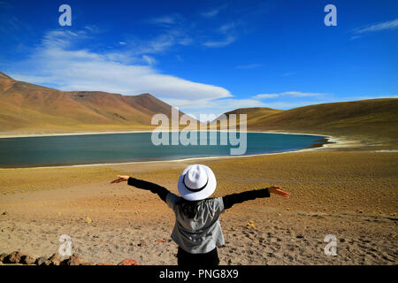 Turista femminile alzando le braccia ammirando il fantastico deep blue lagoon Laguna Miniques, trova nel Altiplano della regione di Antofagasta, Cile Foto Stock