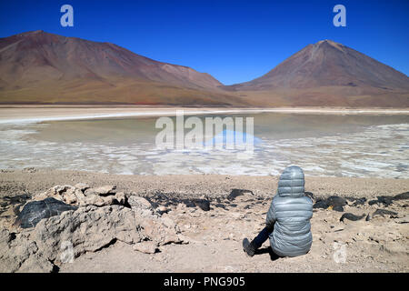 Donna seduta sulla riva in attesa per l'acqua verde effetto della Laguna Verde o il lago verde con il vulcano Lincancabur in sfondo, Potosi, Bolivia Foto Stock