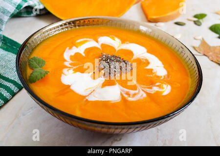 Delicato purea di zucca con panna e chia semi in un nero ciotola di vetro su uno sfondo luminoso. Foto Stock