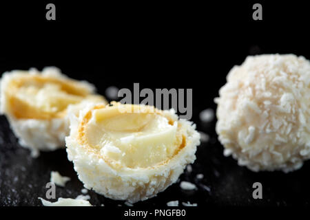 Close up rotto caramella bianco con scaglie di noce di cocco e il cioccolato bianco crema su una di ardesia scura Foto Stock