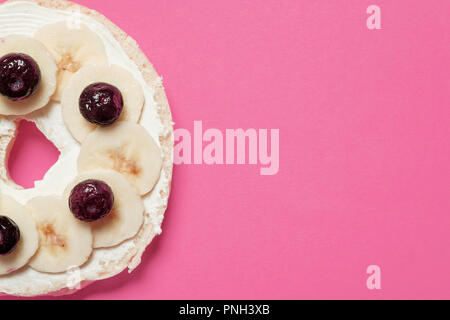 Mezza bagel con formaggio cremoso, mirtilli, e fette di banana su uno sfondo rosa con spazio per la copia e il testo Foto Stock