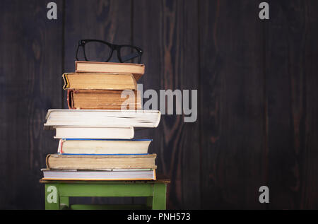 Libri antichi e occhiali su una sedia in legno scuro dello sfondo. Copia dello spazio. Foto Stock