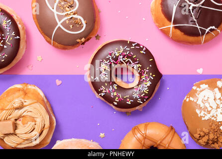 Ciambelle assortite su un gruppo di colore rosa e viola lo sfondo color pastello con un cioccolato classico anello e spruzza le ciambelle nel mezzo. Foto Stock