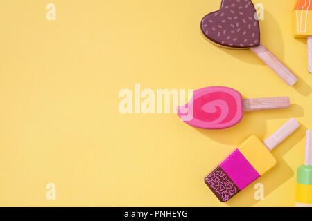 Un assortimento di giocattoli in legno ice lollipop popsicles su sfondo giallo con spazio per la copia e il testo con una composizione di lato, Foto Stock