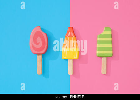 Un assortimento di giocattoli in legno ice lollipop popsicles su un gruppo di colore rosa pastello e blu con spazio per copia e testo Foto Stock