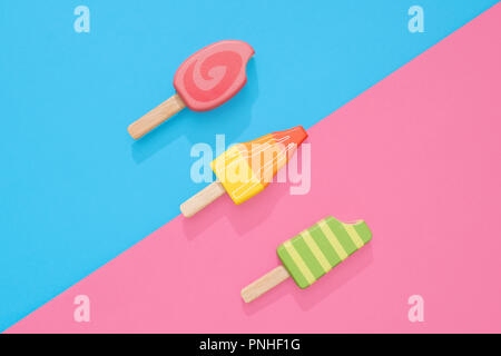 Un assortimento di giocattoli in legno ice lollipop popsicles su un gruppo di colore rosa pastello e blu con spazio per copia e testo Foto Stock