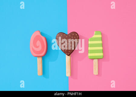 Un assortimento di giocattoli in legno ice lollipop popsicles su un gruppo di colore rosa pastello e blu con spazio per copia e testo Foto Stock