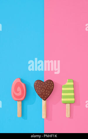 Un assortimento di giocattoli in legno ice lollipop popsicles su un gruppo di colore rosa pastello e blu con spazio per copia e testo Foto Stock