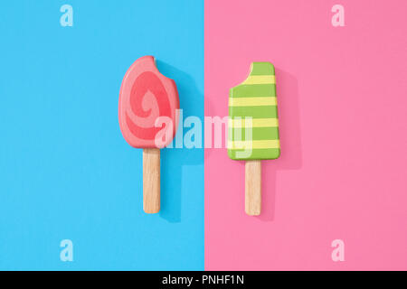 Un assortimento di giocattoli in legno ice lollipop popsicles su un gruppo di colore rosa pastello e blu con spazio per copia e testo Foto Stock