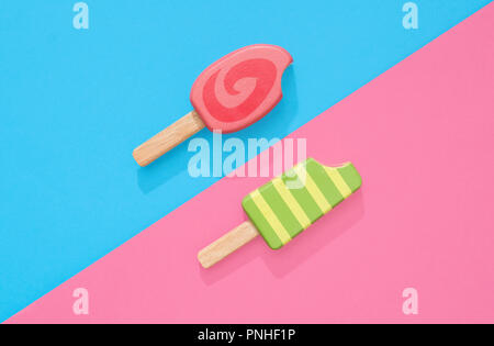 Un assortimento di giocattoli in legno ice lollipop popsicles su un gruppo di colore rosa pastello e blu con spazio per copia e testo Foto Stock