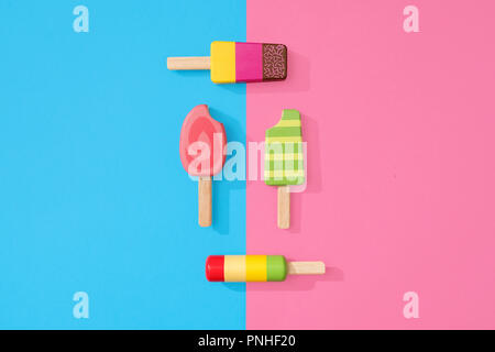 Un assortimento di giocattoli in legno ice lollipop popsicles su un gruppo di colore rosa pastello e blu con spazio per copia e testo Foto Stock