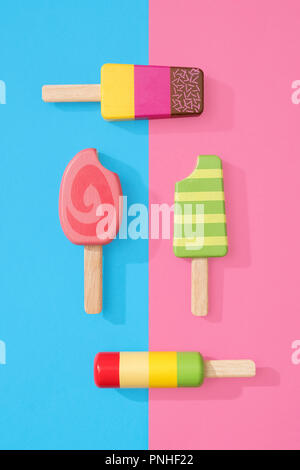 Un assortimento di giocattoli in legno ice lollipop popsicles su un gruppo di colore rosa pastello e blu con spazio per copia e testo Foto Stock