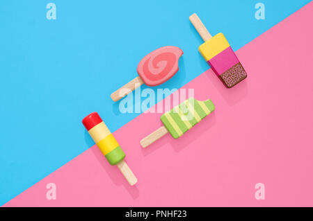 Un assortimento di giocattoli in legno ice lollipop popsicles su un gruppo di colore rosa pastello e blu con spazio per copia e testo Foto Stock