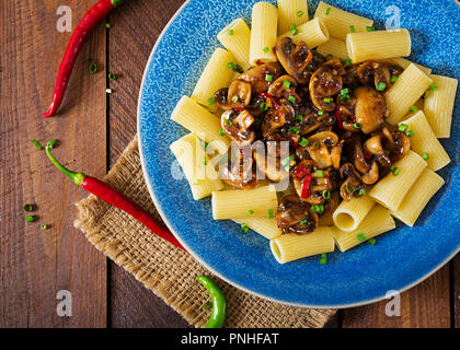 Pasta Vegetariana rigatoni con funghi e peperoncino in vaso blu su un tavolo di legno. Cibo vegan. Lay piatto. Vista superiore Foto Stock