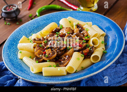 Pasta Vegetariana rigatoni con funghi e peperoncino in vaso blu su un tavolo di legno. Cibo vegan. Foto Stock