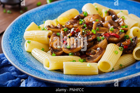 Pasta Vegetariana rigatoni con funghi e peperoncino in vaso blu su un tavolo di legno. Cibo vegan. Foto Stock