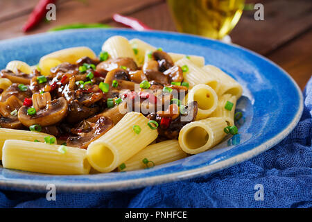 Pasta Vegetariana rigatoni con funghi e peperoncino in vaso blu su un tavolo di legno. Cibo vegan. Foto Stock
