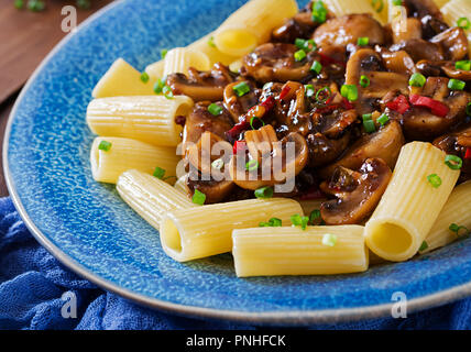Pasta Vegetariana rigatoni con funghi e peperoncino in vaso blu su un tavolo di legno. Cibo vegan. Foto Stock