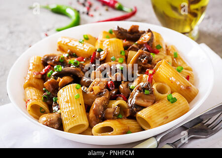 Pasta Vegetariana rigatoni con funghi e peperoncino in vaso bianco sulla tabella grigia. Cibo vegan. Foto Stock