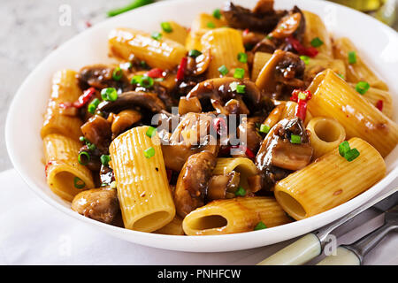 Pasta Vegetariana rigatoni con funghi e peperoncino in vaso bianco sulla tabella grigia. Cibo vegan. Foto Stock