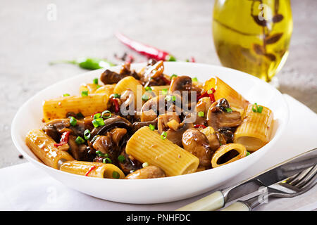 Pasta Vegetariana rigatoni con funghi e peperoncino in vaso bianco sulla tabella grigia. Cibo vegan. Foto Stock