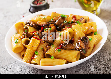 Pasta Vegetariana rigatoni con funghi e peperoncino in vaso bianco sulla tabella grigia. Cibo vegan. Foto Stock