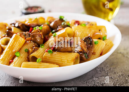 Pasta Vegetariana rigatoni con funghi e peperoncino in vaso bianco sulla tabella grigia. Cibo vegan. Foto Stock