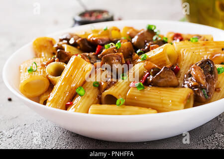Pasta Vegetariana rigatoni con funghi e peperoncino in vaso bianco sulla tabella grigia. Cibo vegan. Foto Stock