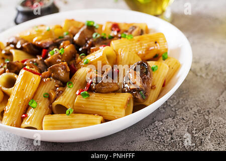 Pasta Vegetariana rigatoni con funghi e peperoncino in vaso bianco sulla tabella grigia. Cibo vegan. Foto Stock