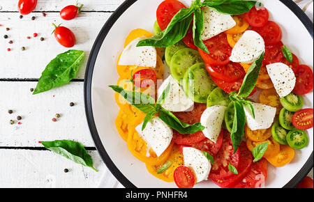Mozzarella, pomodoro e basilico foglie di erbe nella piastra sul bianco tavolo in legno. Insalata caprese. Il cibo italiano. Vista superiore Foto Stock