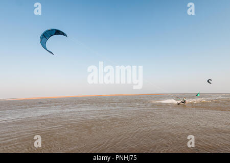 Kiteboarder tirando i trucchi e ottenere aria su una luminosa giornata d'estate con perfetto cielo blu chiaro. Strret shingle, Suffolk, Regno Unito Foto Stock