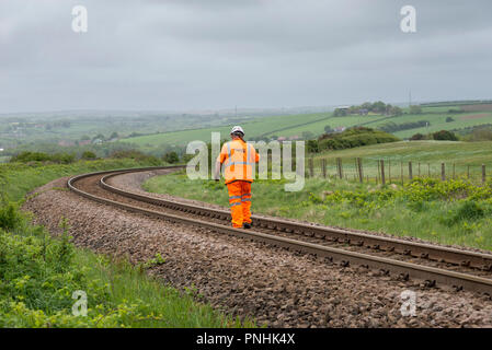 Operaio ferroviario in arancione abiti da lavoro a piedi lungo la linea a Skinningrove, North Yorkshire. Foto Stock