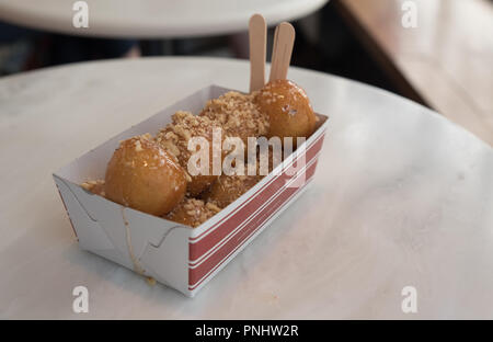 Lukamades, impasto fritto di palline in una carta estrarre il piatto con due cucchiai di legno ricoperti di miele e i dadi su un marmo bianco tabella Foto Stock