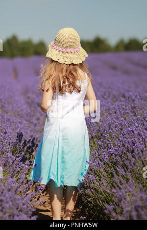 Bambina in piedi in una lavanda archiviato indossando un cappello su un giorno d'estate. Foto Stock