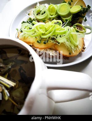 Chiusura del sandwich vegetariano.Tutto il pane di grano, pecorino, porro, burro, germogli, germogli e la tazza di tè di montagna, pastore la tea in cat mug Foto Stock