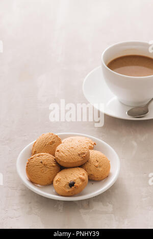 Il caffè. Porcellana Bianca tazza di caffè appena fatto top view close-up disposti con biscotti, cucchiaio e piastra su sfondo chiaro Foto Stock