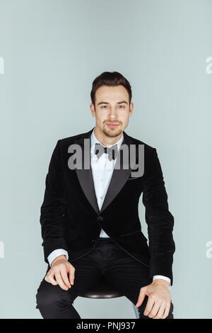 Ritratto di un giovane uomo bello in uno smoking, guardando la telecamera, contro pl​ain di sfondo per studio. Foto Stock