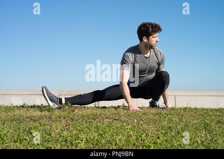 L uomo si allunga la gamba nel terreno in erba Foto Stock