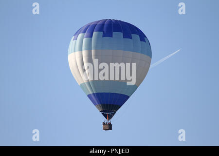 Blu e bianco mongolfiera in volo con le fiammelle innalzantisi nella calotta battenti vicino a Montecassiano, Italia un piano dietro con il sentiero di vapore Foto Stock